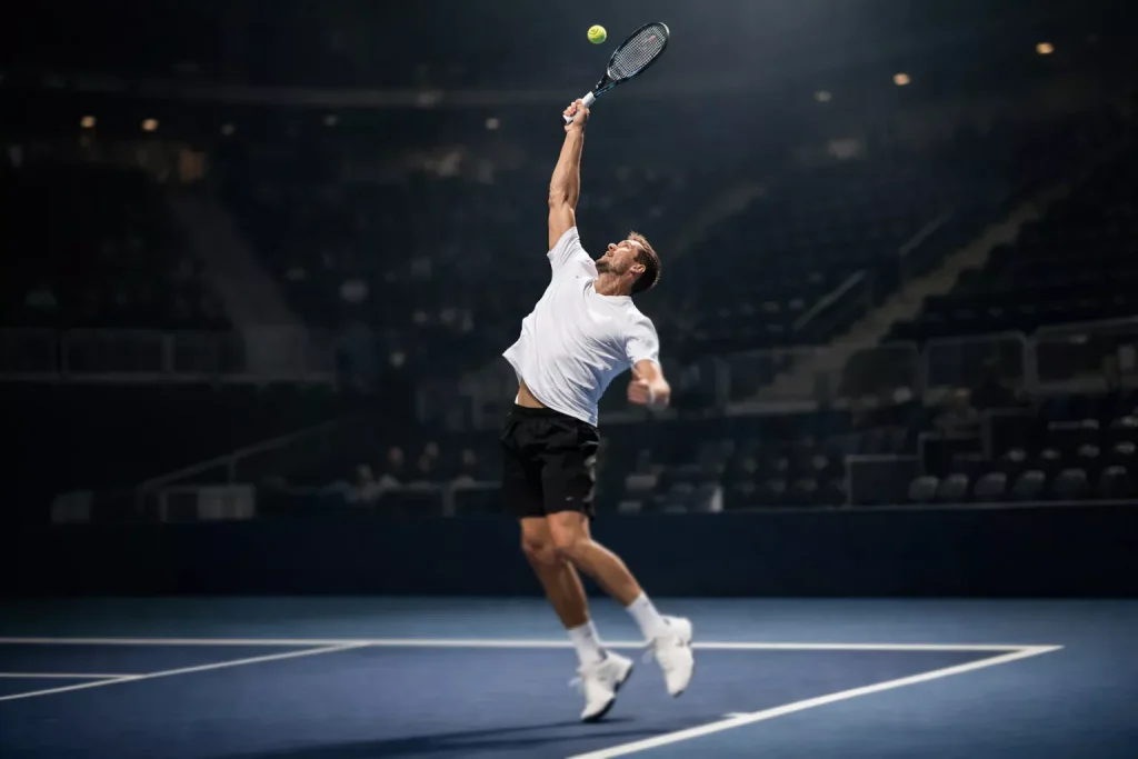 Großer Tennisspieler beim kraftvollen Aufschlag auf Indoor-Hartplatz